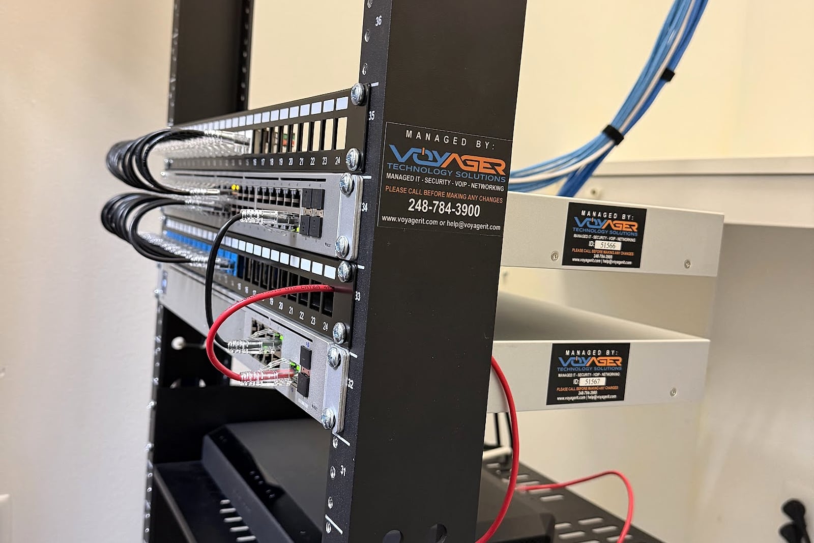 Commercial network rack with switches, patch panels, and Voyager service labels.