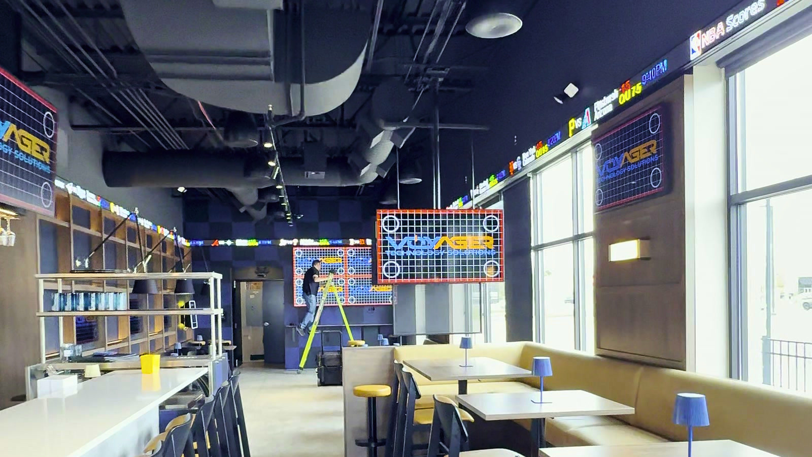 Finished restaurant interior with Voyager-branded displays and an installer at work.