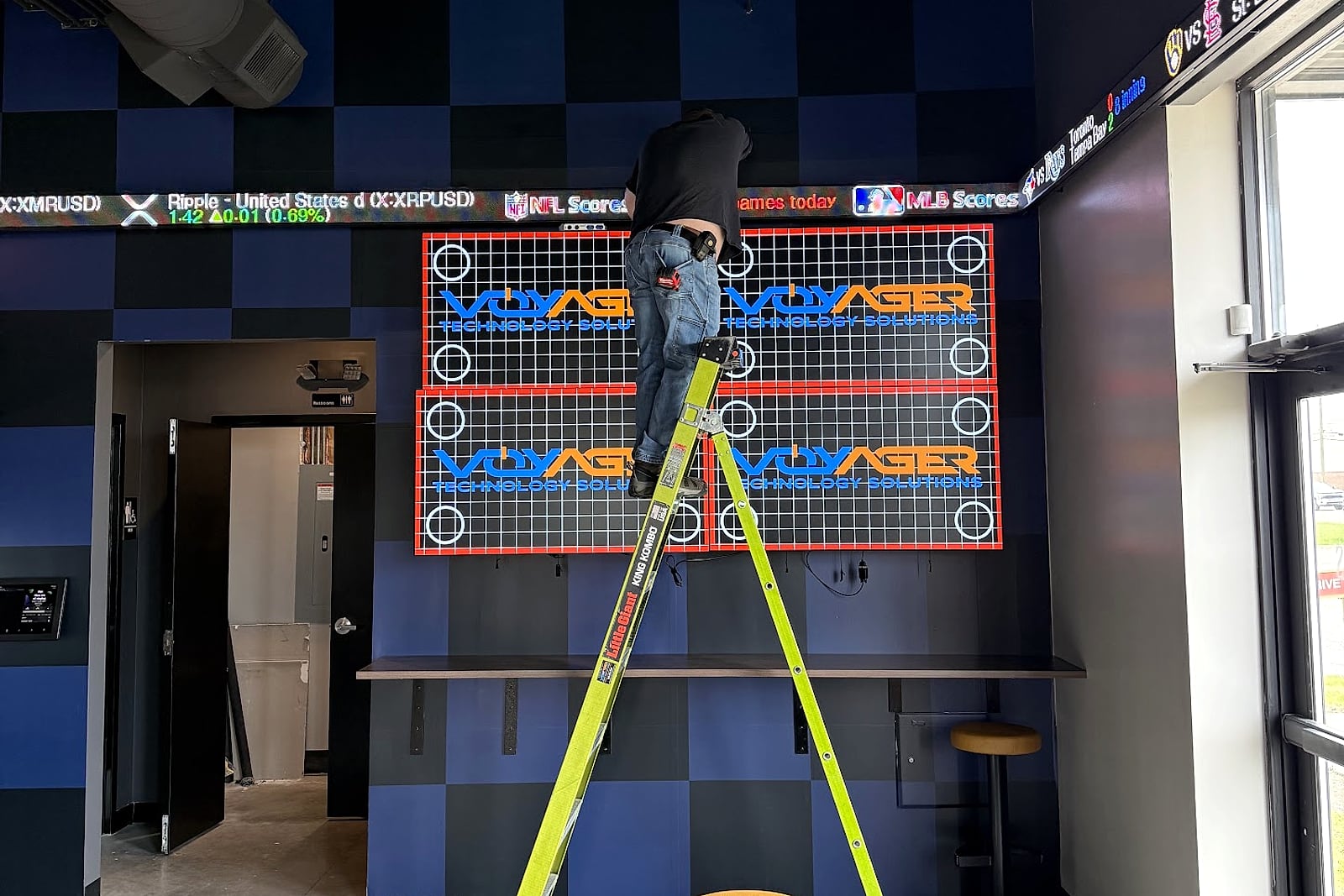 Technician working from a ladder on a Voyager-branded display installation.